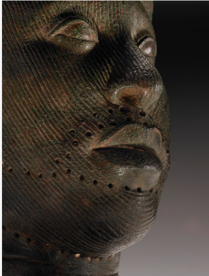 Close-up of a sculpted metal head with fine facial lines and holes around the mouth.