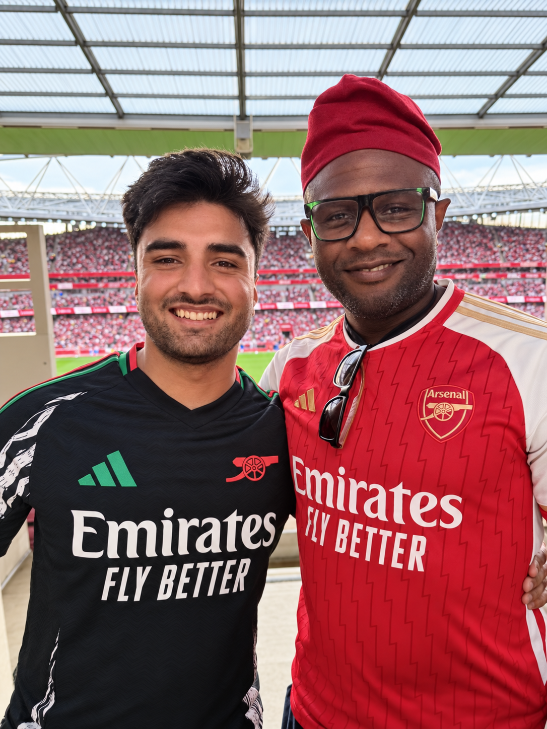 Cornitto Tiger and Ọlálékan smiling in Arsenal shirts inside the Emirates Stadium, with the crowd behind them