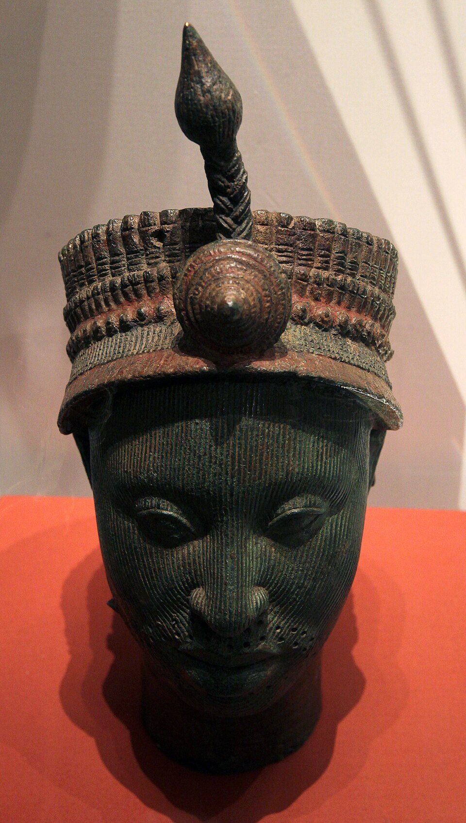Close view of an Ilé-Ifẹ̀ brass head with fine facial lines and an elaborate crown topped by a plume.