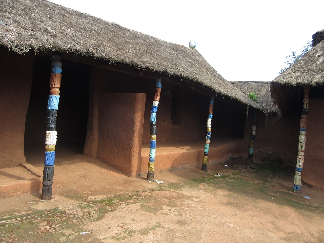 A thatched museum courtyard structure with carved and coloured pillars.